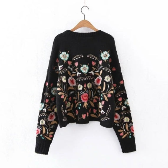 Black sweater with floral embroidery on a hanger against a white background