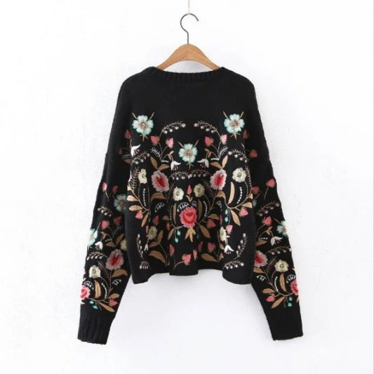 Black sweater with floral embroidery on a hanger against a white background