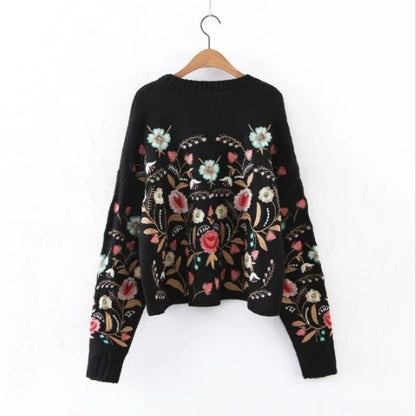 Black sweater with floral embroidery on a hanger against a white background